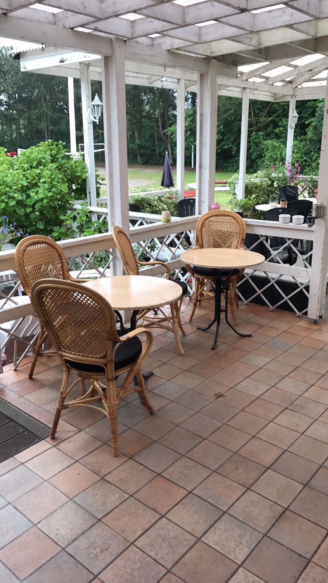 En overdækket patio med to runde borde og fletstole.