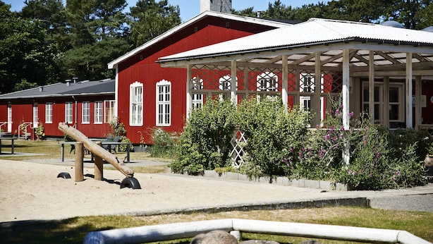 Un bâtiment rouge doté d’un porche abrité, d’une balançoire et d’un petit jardin.
