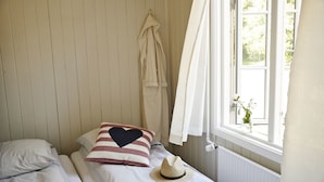 Une chambre avec deux lits, une fenêtre avec des rideaux, un radiateur et un chapeau posé sur l’un des lits.