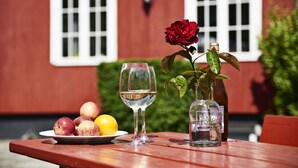 Une table avec une assiette de pommes et un citron, un verre d’eau, une bouteille de vin et un vase contenant une rose.