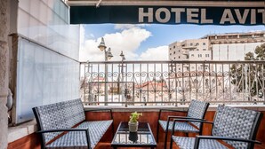 A balcony with four wicker chairs, a small table with a potted plant, and a view of buildings and a clear sky. - Avital Hotel (Jerusalem)