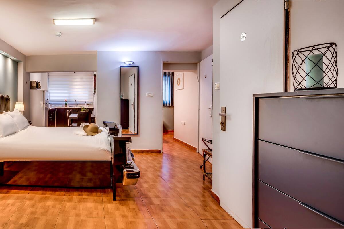 A hotel room with a bed, bedside table, lamp, and a large painting of a car on the wall.