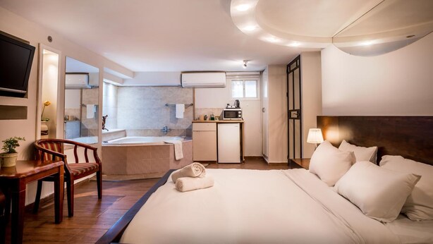 A hotel room with a bed, a desk, a chair, a small kitchenette, a bathroom with a bathtub, and a TV mounted on the wall. - Avital Hotel (Jerusalem)