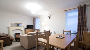 A cozy living room with a fireplace, sofa, and dining table. - Blair Drummond Holiday Home (Doune)