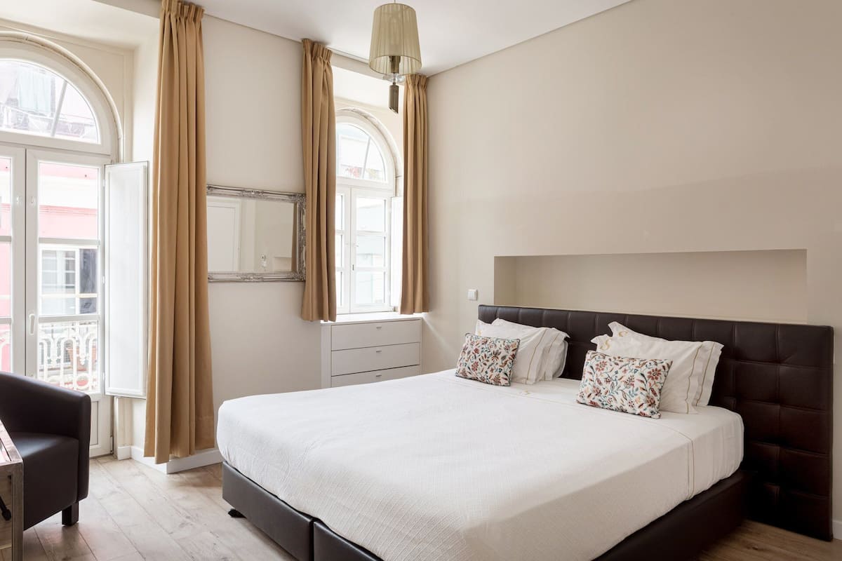 A bedroom with a large bed, a nightstand, a chair, and a window with curtains.