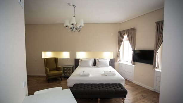 A hotel room with a bed, bedside lamps, a chair, a TV, and a wooden floor. - Sui7es Guest House Cascais (Cascais)