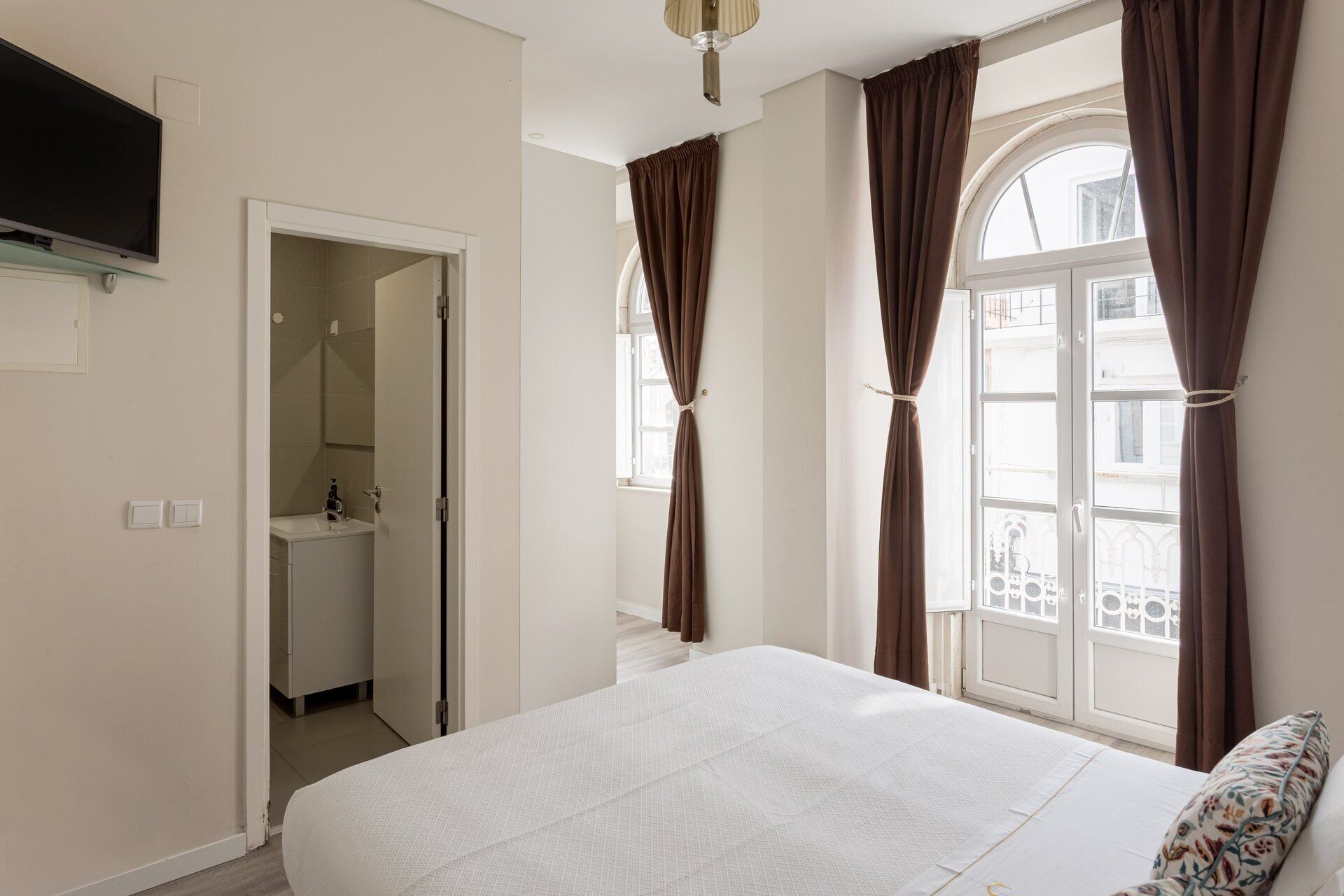 Une chambre à coucher avec un lit, une télévision, une salle de bain et une fenêtre avec des rideaux.