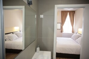 Une chambre d’hôtel avec un grand miroir, un lit, une table de chevet, une commode et une fenêtre avec des rideaux.