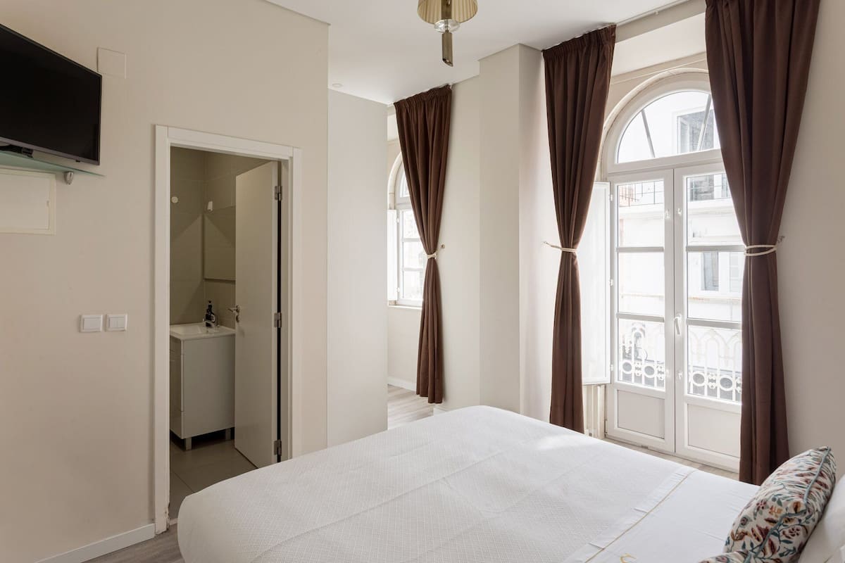 A bedroom with a bed, a TV, a bathroom, and a window with curtains.