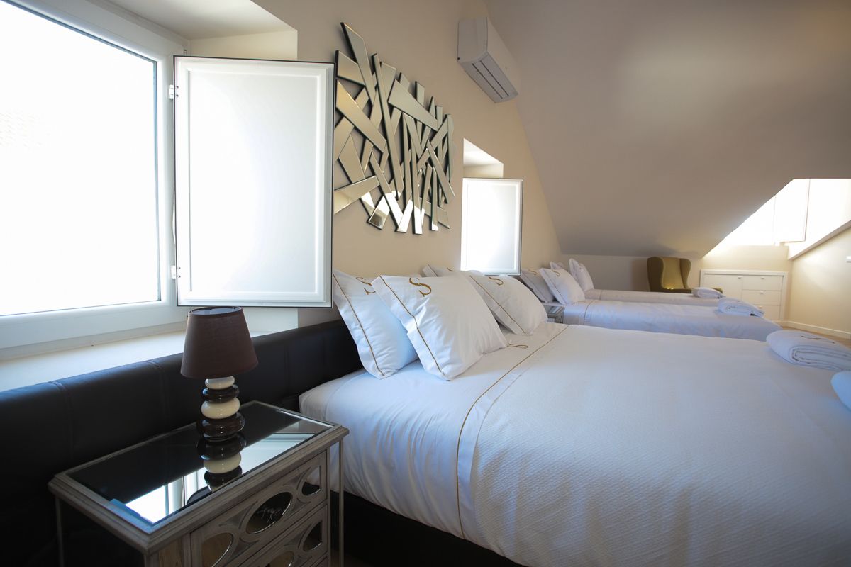 A hotel room with two beds, a bedside table with a lamp, a decorative wall piece, and a window.