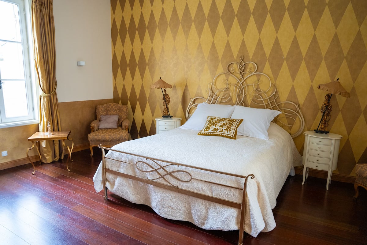 A neatly arranged bedroom with a large bed, two bedside tables, a chair, and a window with curtains.