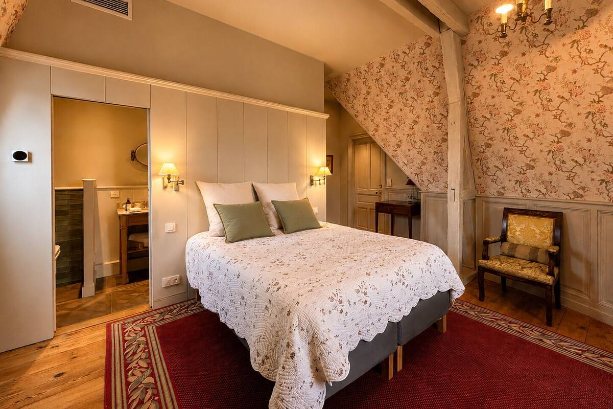 A bedroom with a bed, a chair, a bathroom, and a staircase.
