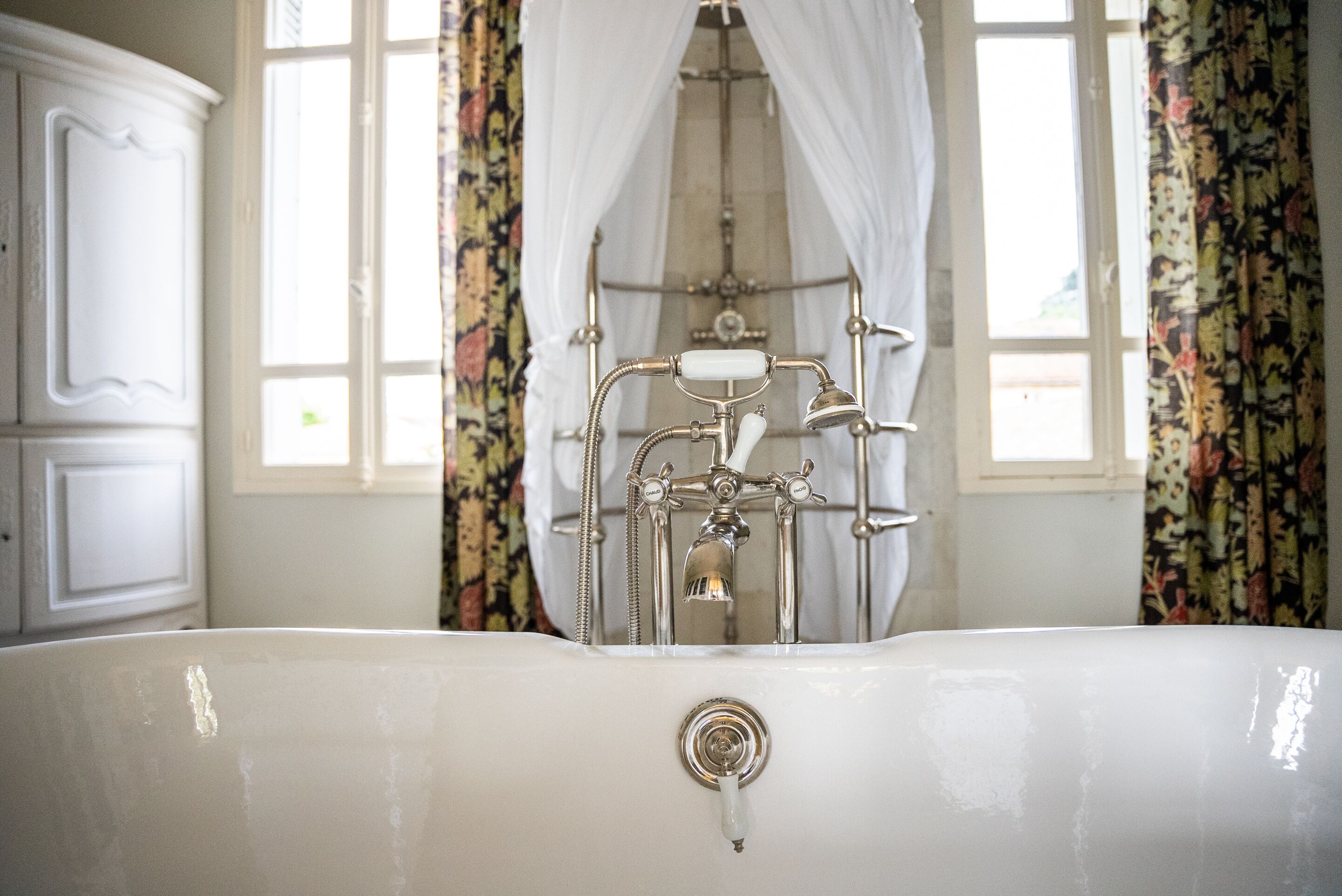 A bathroom with a large bathtub, a shower with a curtain, and floral-patterned curtains.