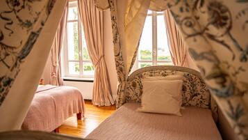 Un dormitorio con dos camas, cortinas con estampado floral y vista a zonas verdes.
