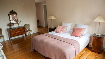 A bedroom with a large bed, wooden floor, a dresser, a mirror, and two bedside tables with lamps.