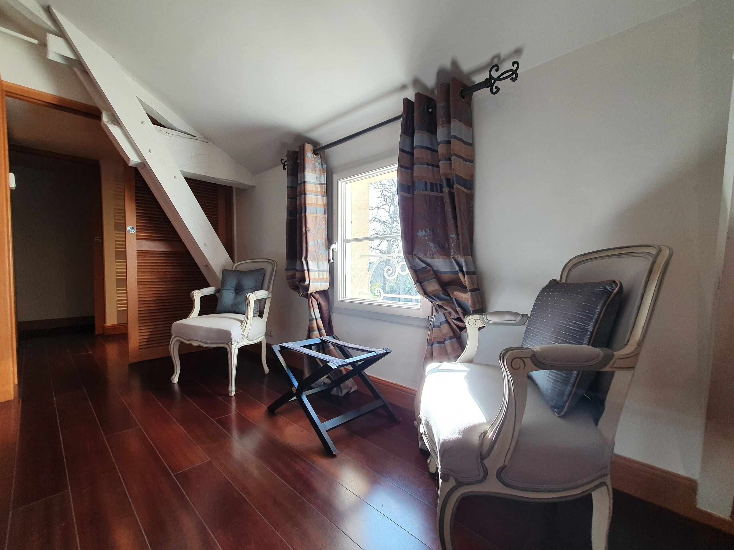 Una habitación con dos sillones, una mesita y un ventanal con cortinas.
