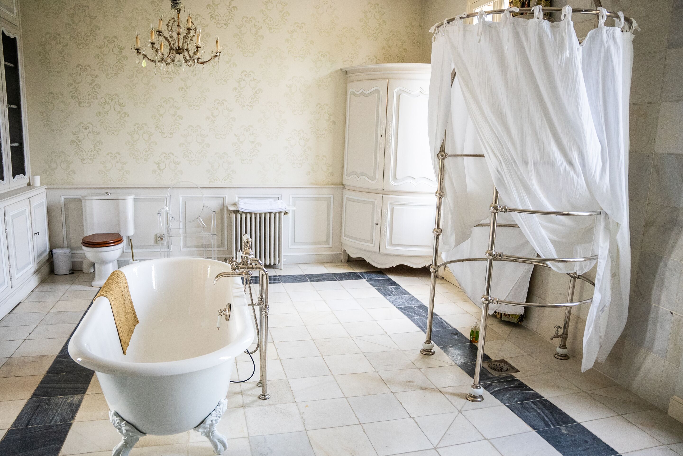 Ein Badezimmer mit freistehender Badewanne, einem weißen Schrank, einem Heizkörper und einer Kristallleuchter.