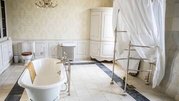 Ein Badezimmer mit freistehender Badewanne, einem weißen Schrank, einem Heizkörper und einer Kristallleuchter.