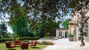 A courtyard with a paved walkway, red wicker chairs, and a building with arched windows. - Chambre D'hôtes Château de Lussac (Lussac)