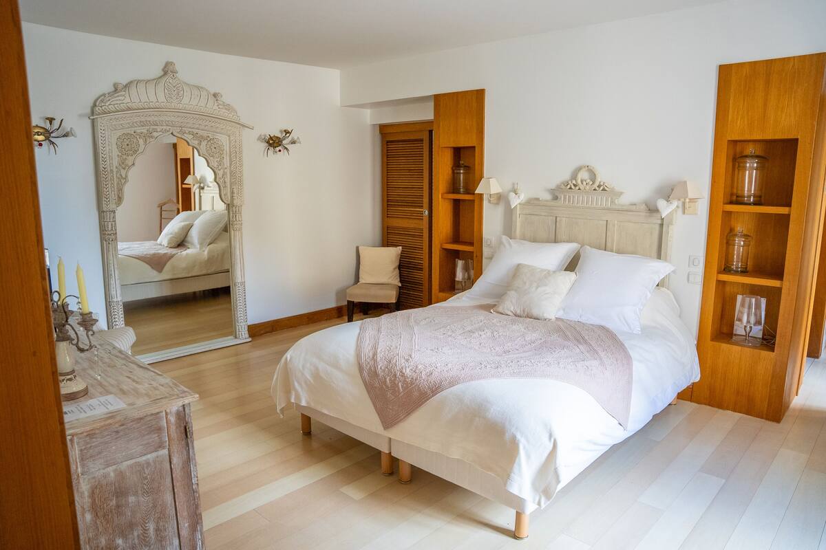 A bedroom with a large bed, a wooden wardrobe, a mirror, and a small table with candles.