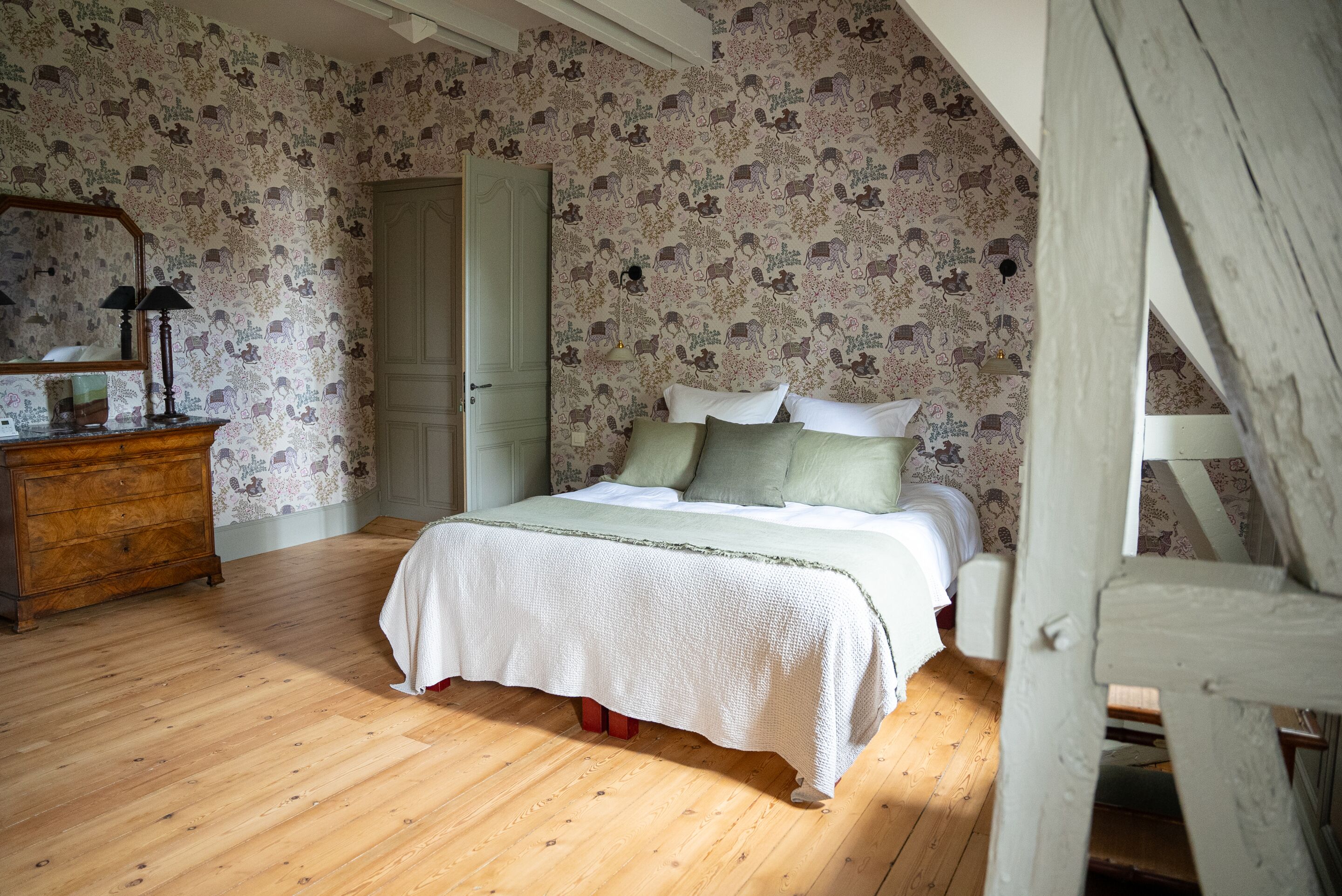 Un dormitorio con piso de madera, una cama con ropa de cama blanca, un aparador y un espejo.