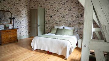 Un dormitorio con piso de madera, una cama con ropa de cama blanca, un aparador y un espejo.