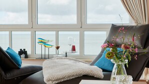 Uma sala de estar moderna com vista para o mar, com um sofá, um cobertor branco, um vaso com flores e binóculos em um peitoris.