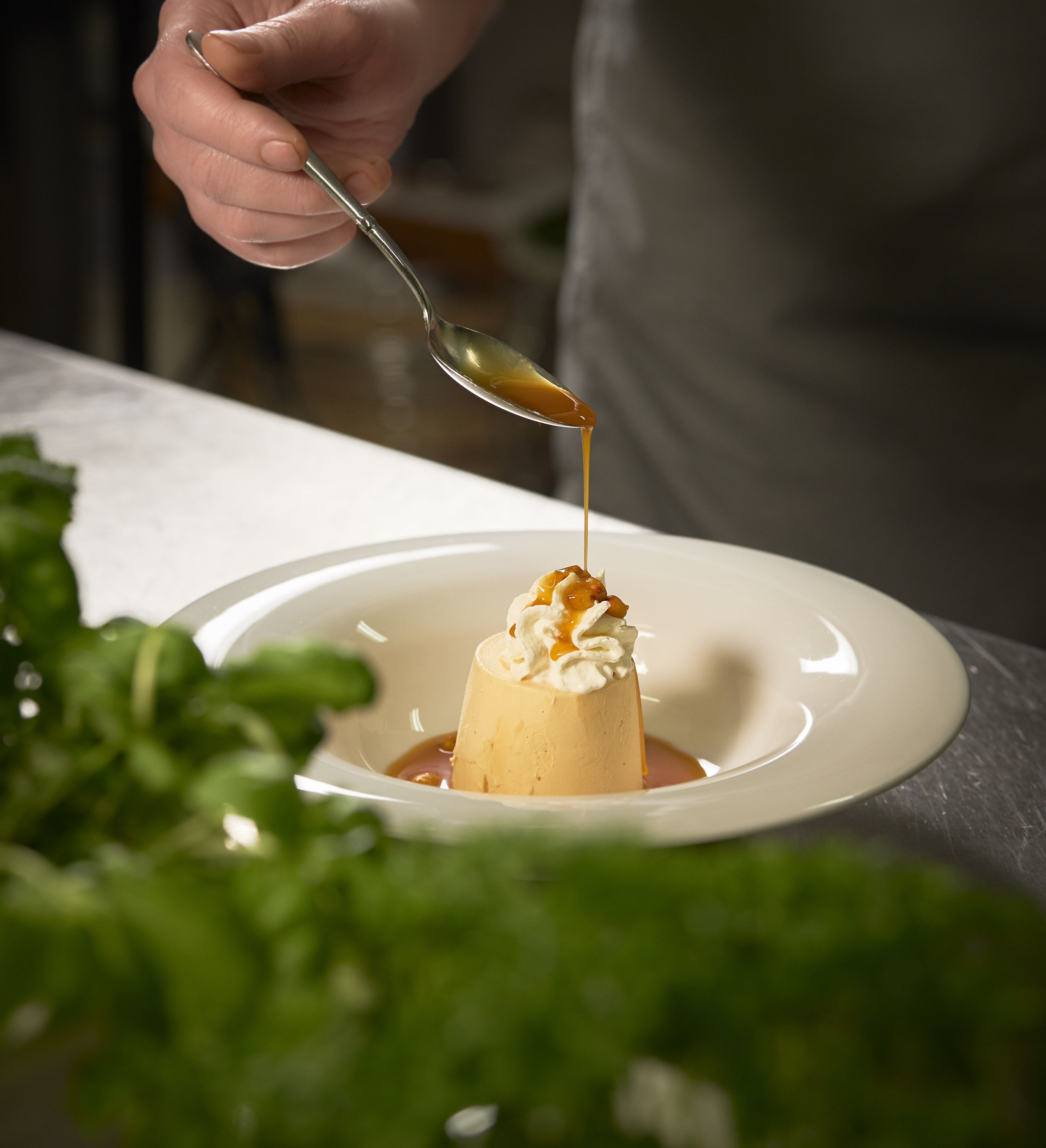 A dessert on a plate with a spoon pouring sauce over it.