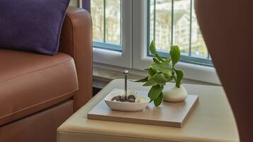 A living room with a brown leather sofa, a small table with a plant and a bowl of fruit, and a view of the sea through a balcony railing.