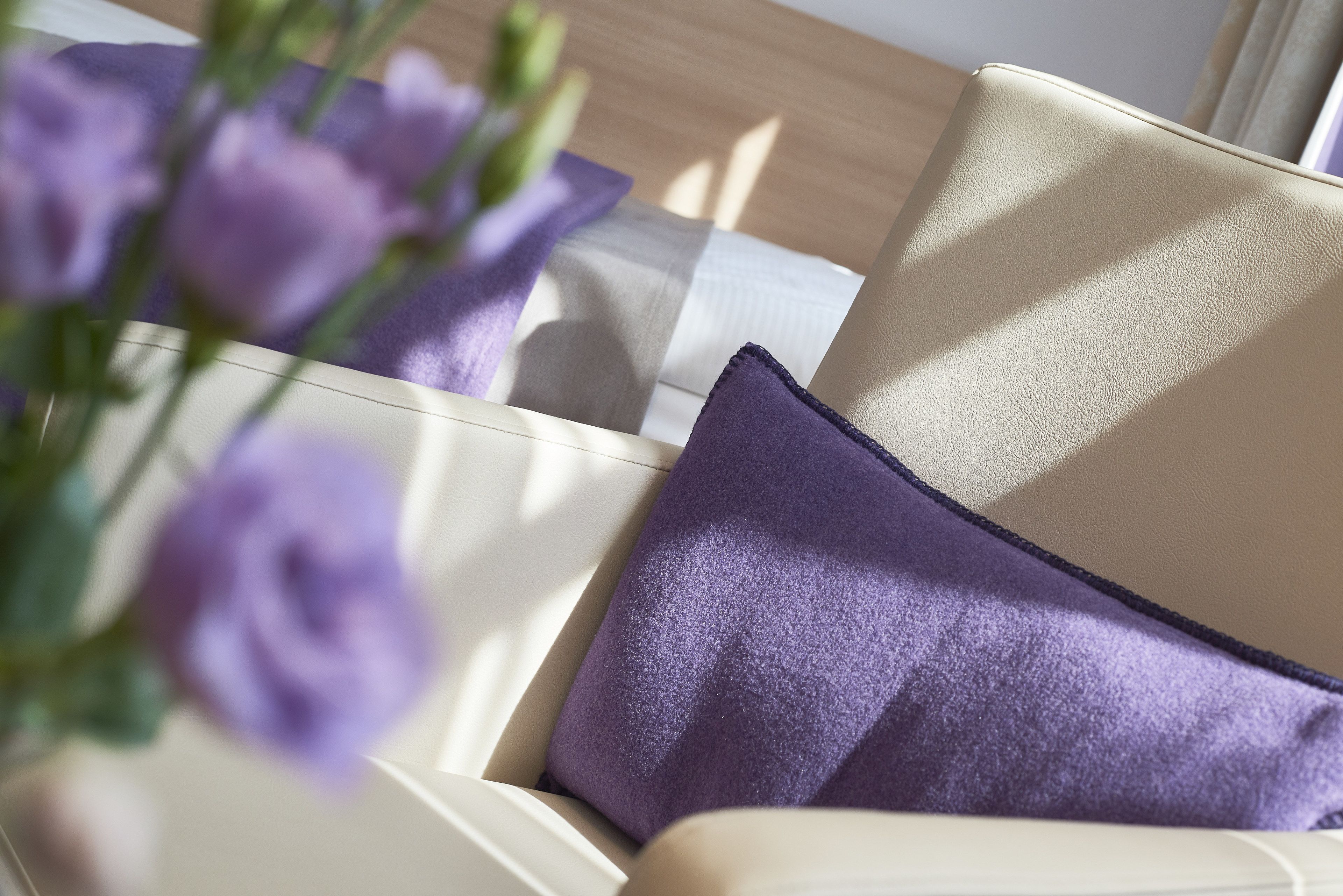 Un sofá color crema con un cojín morado y un ramo de flores moradas.