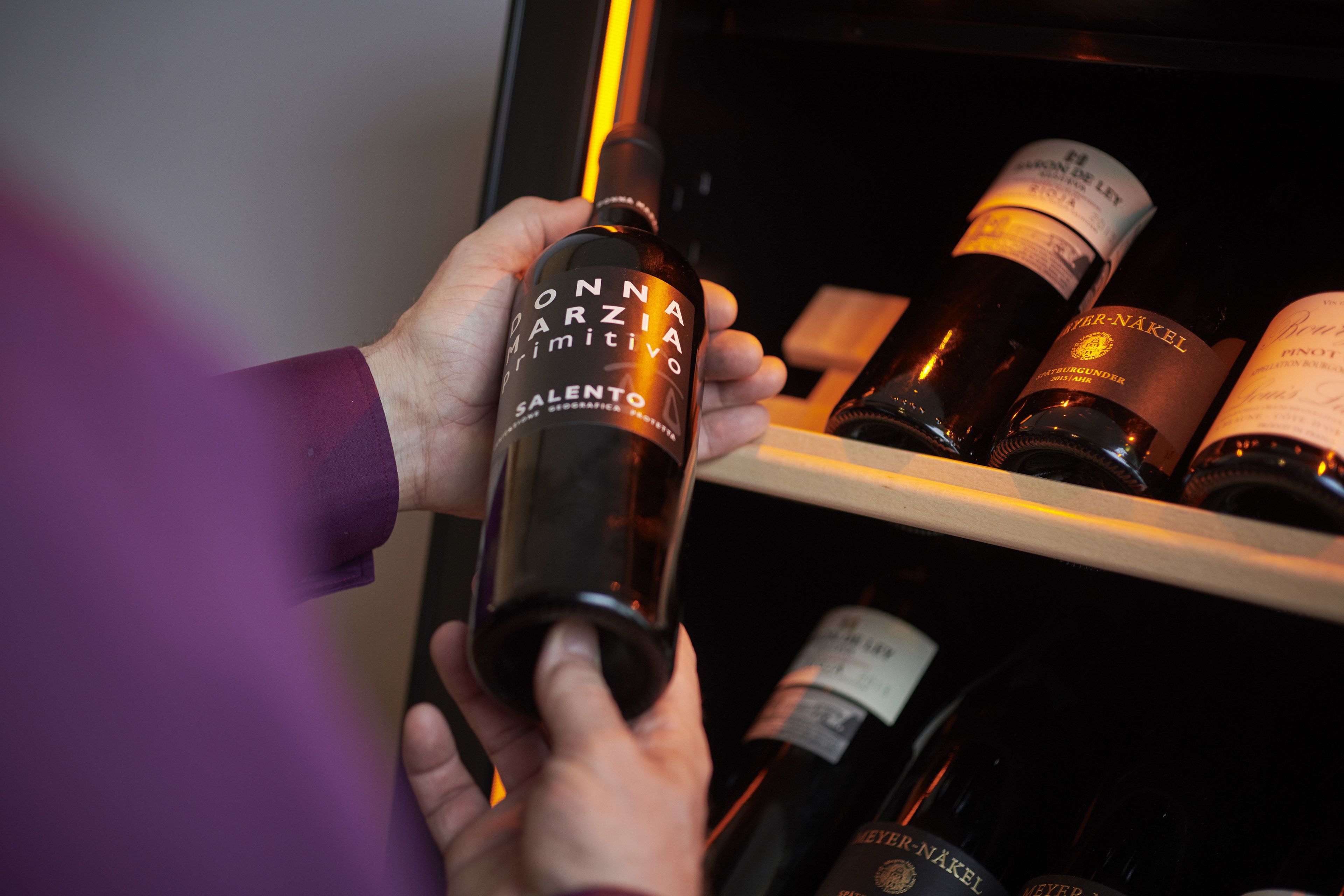 Una persona sosteniendo una botella de vino con la etiqueta que dice "ONNAAIARZIMITIVO SALENTO".