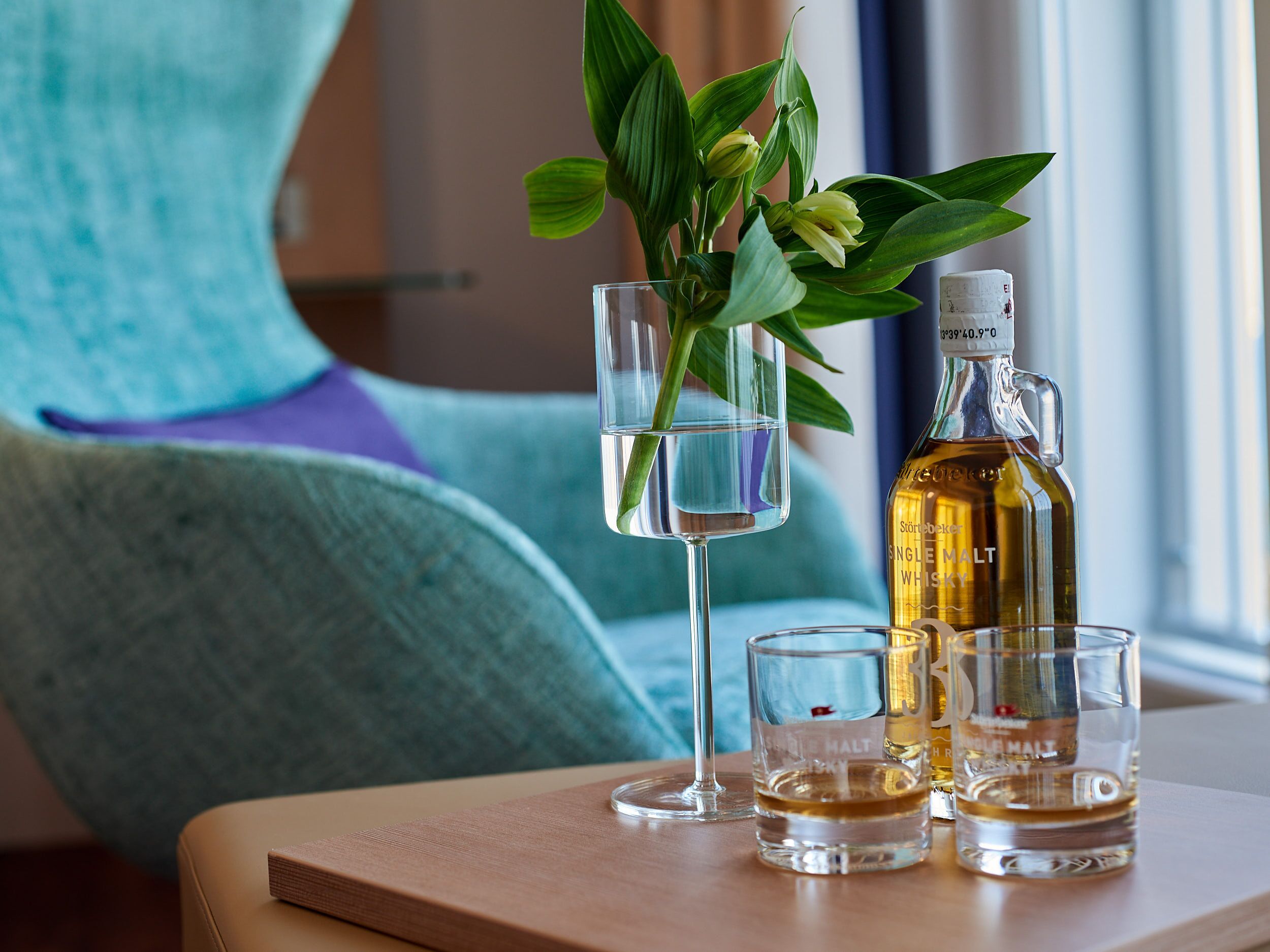 A table with a bottle of single malt whiskey, two shot glasses, and a glass with a flower arrangement.