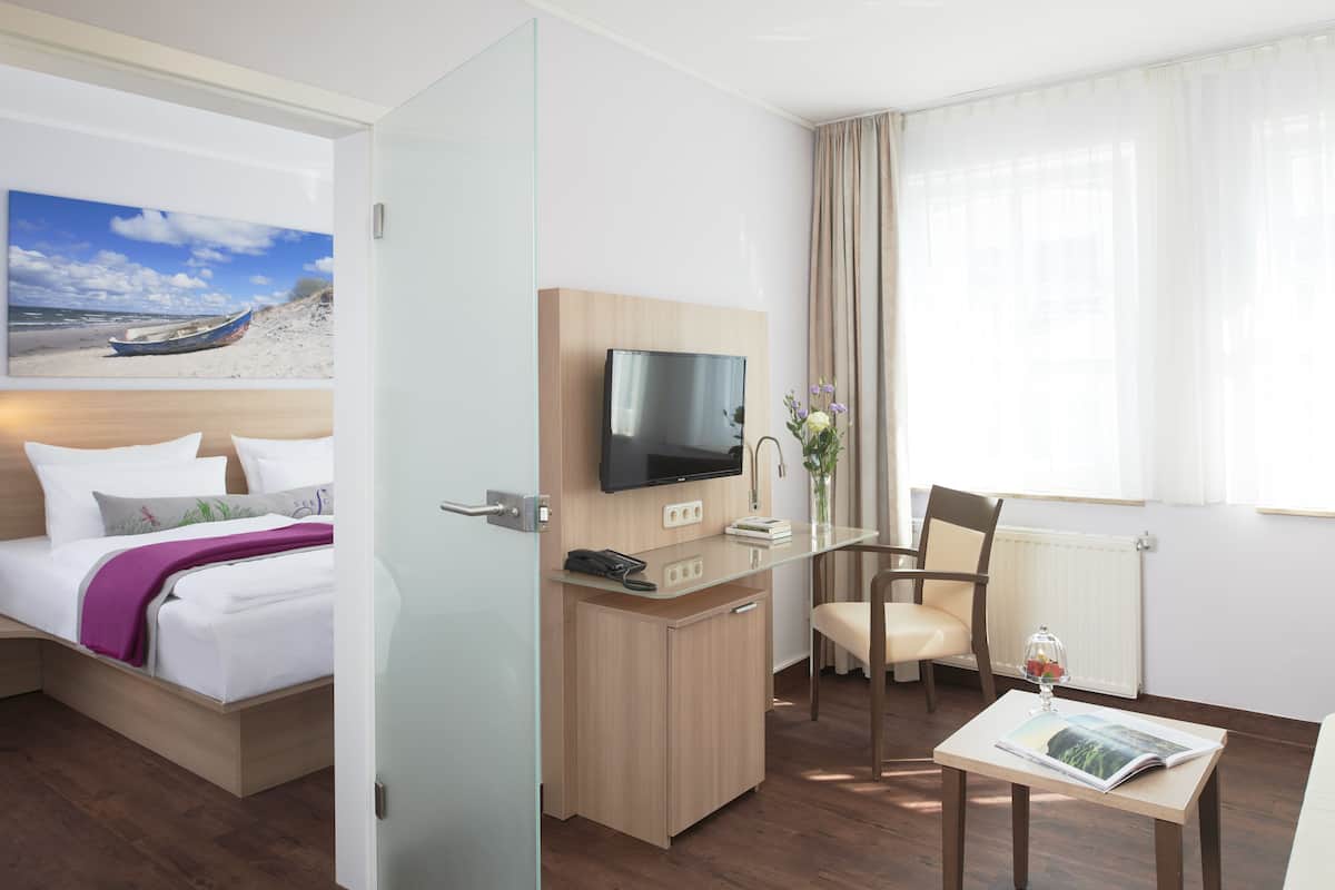 A hotel room with a bed, a desk, a chair, a TV, and a window with curtains.