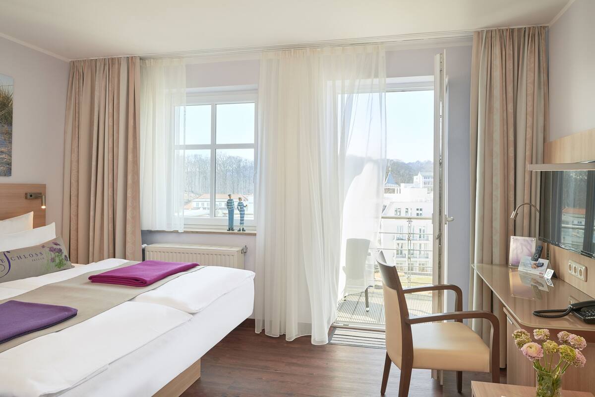 A hotel room with a bed, a desk, a chair, and a view of the city.