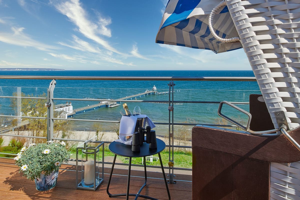 A balcony with a view of the sea, a table with binoculars, a bottle of champagne, and a flower arrangement.