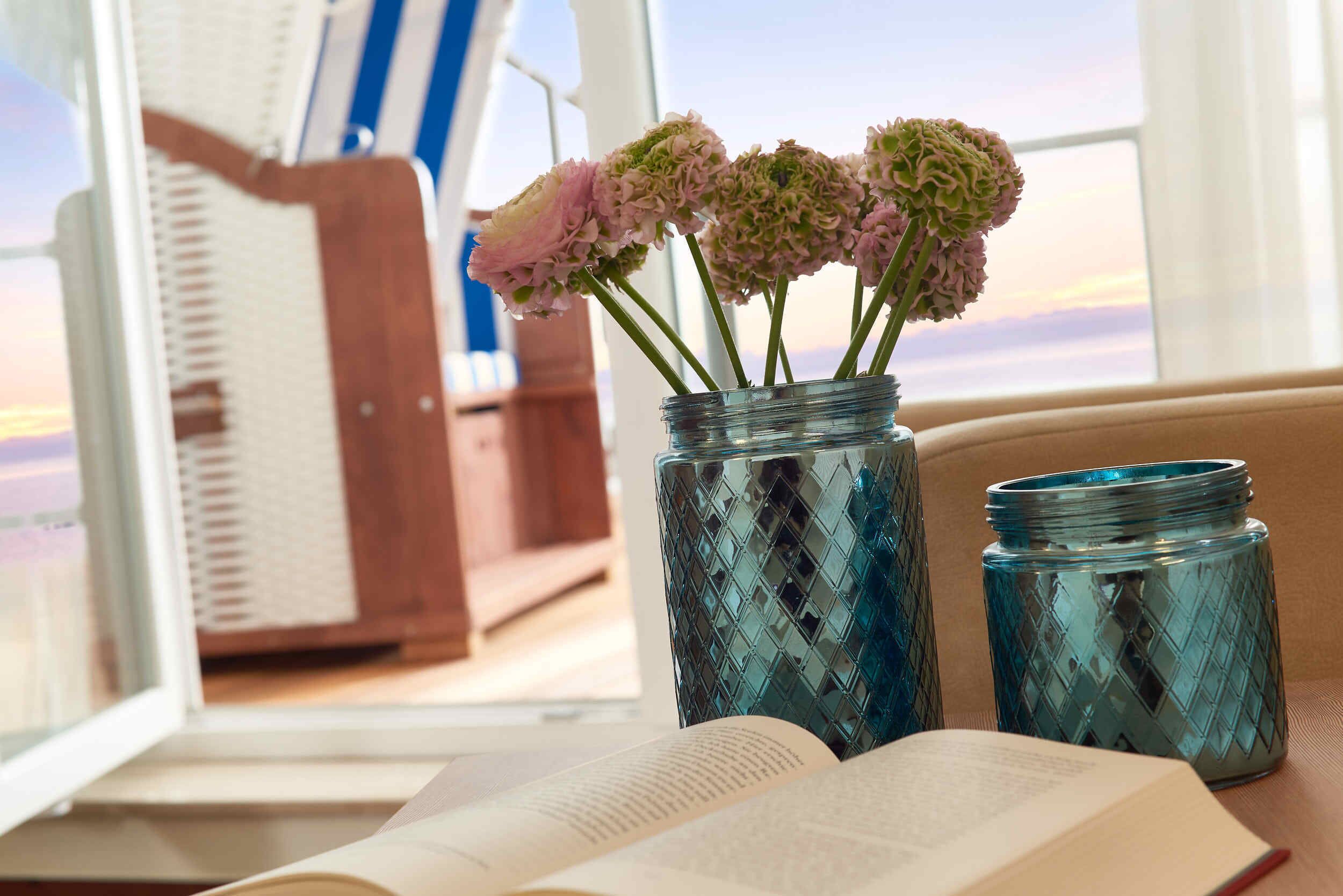 An open book on a table with two glass jars containing flowers.
