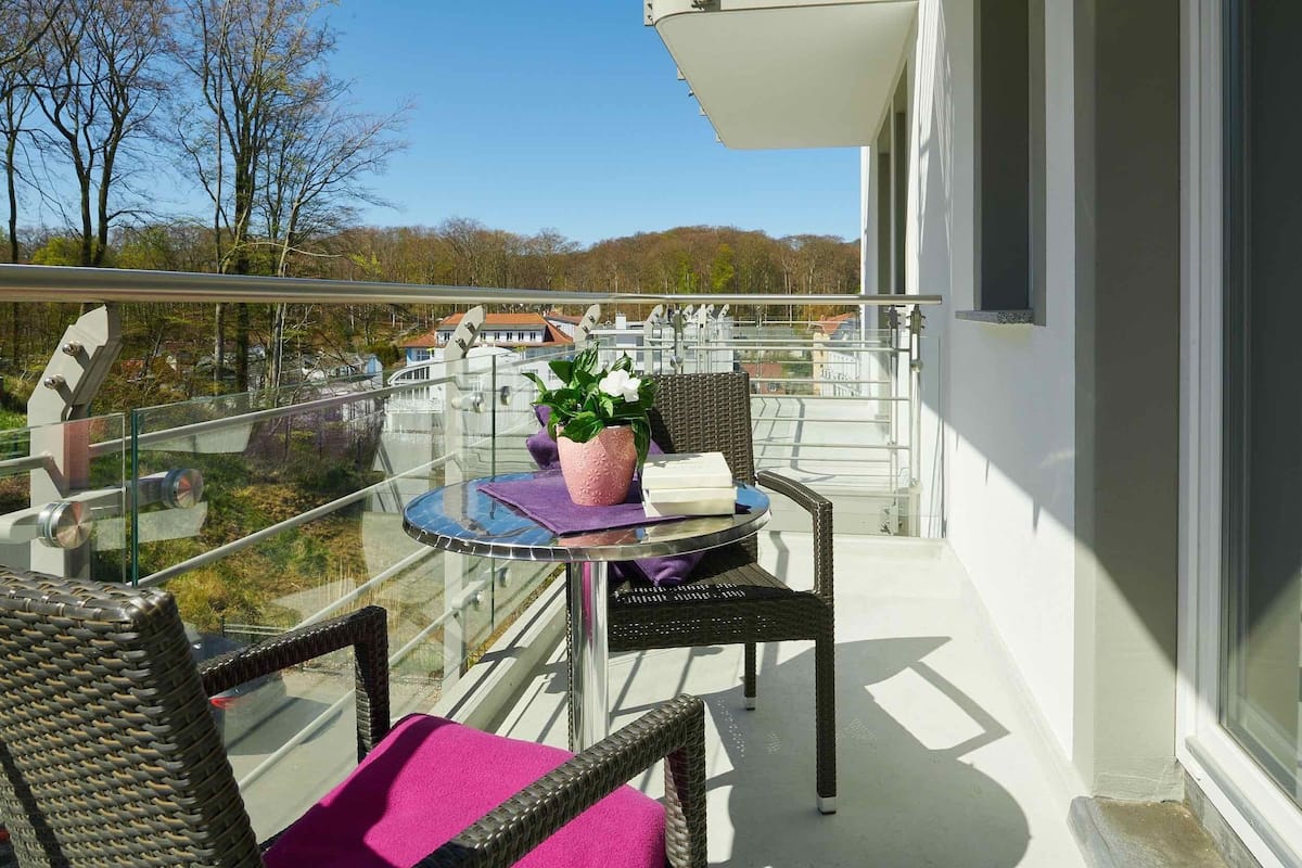 A balcony with wicker chairs, a glass table, and a potted plant.