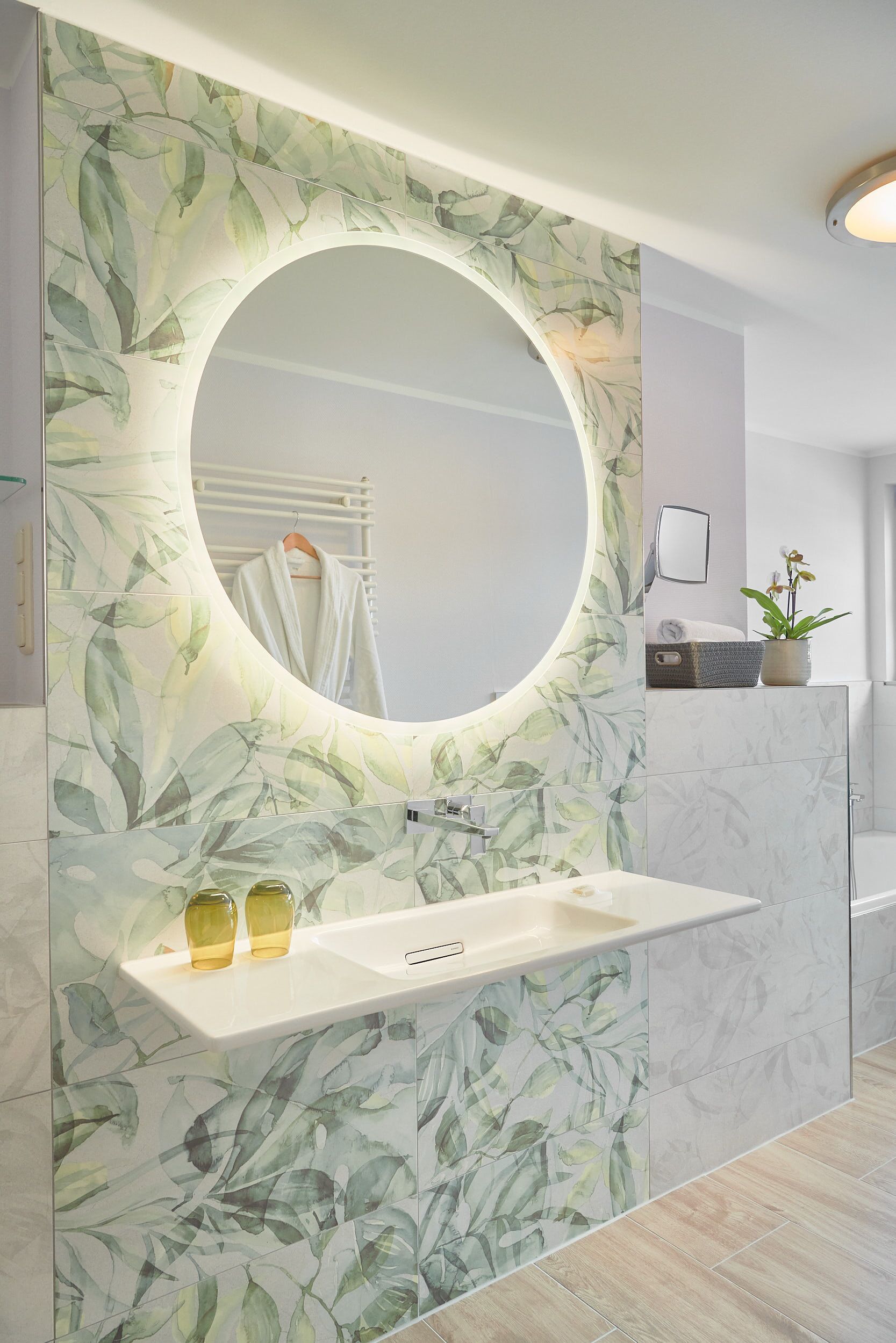 A bathroom with a round mirror, a sink, and a plant.