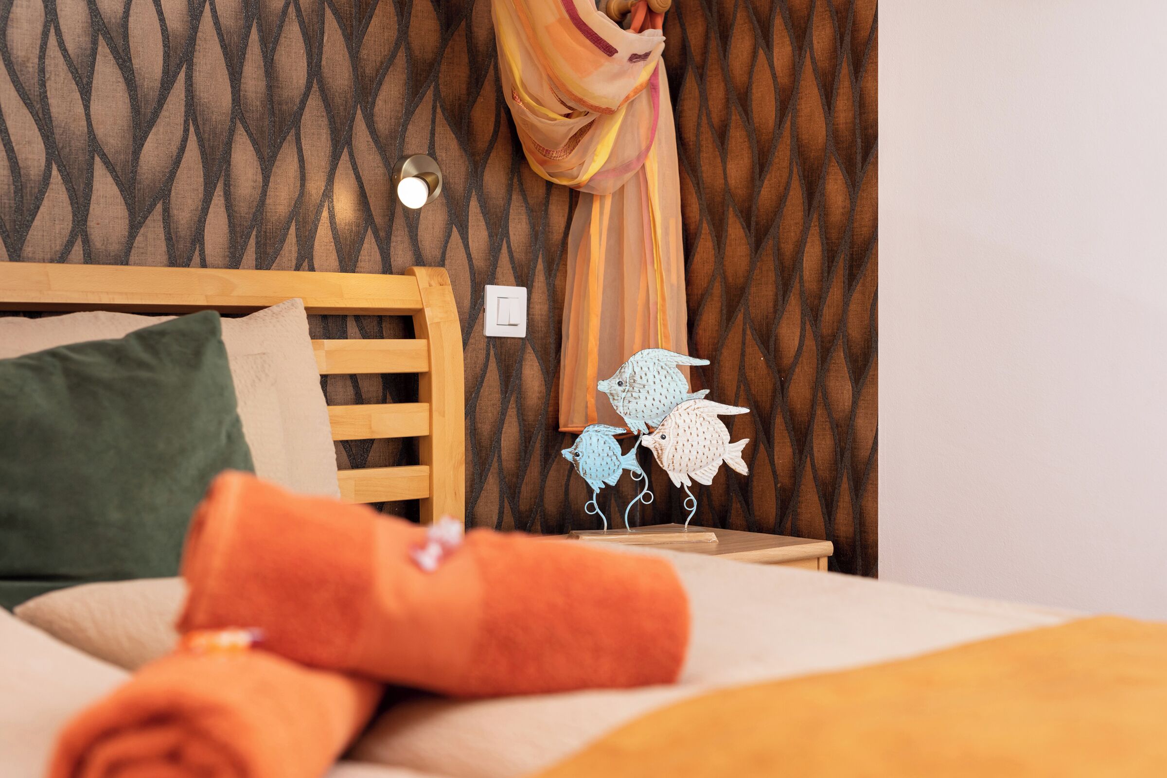 A neatly made bed with a green pillow, an orange towel, and a wooden headboard.