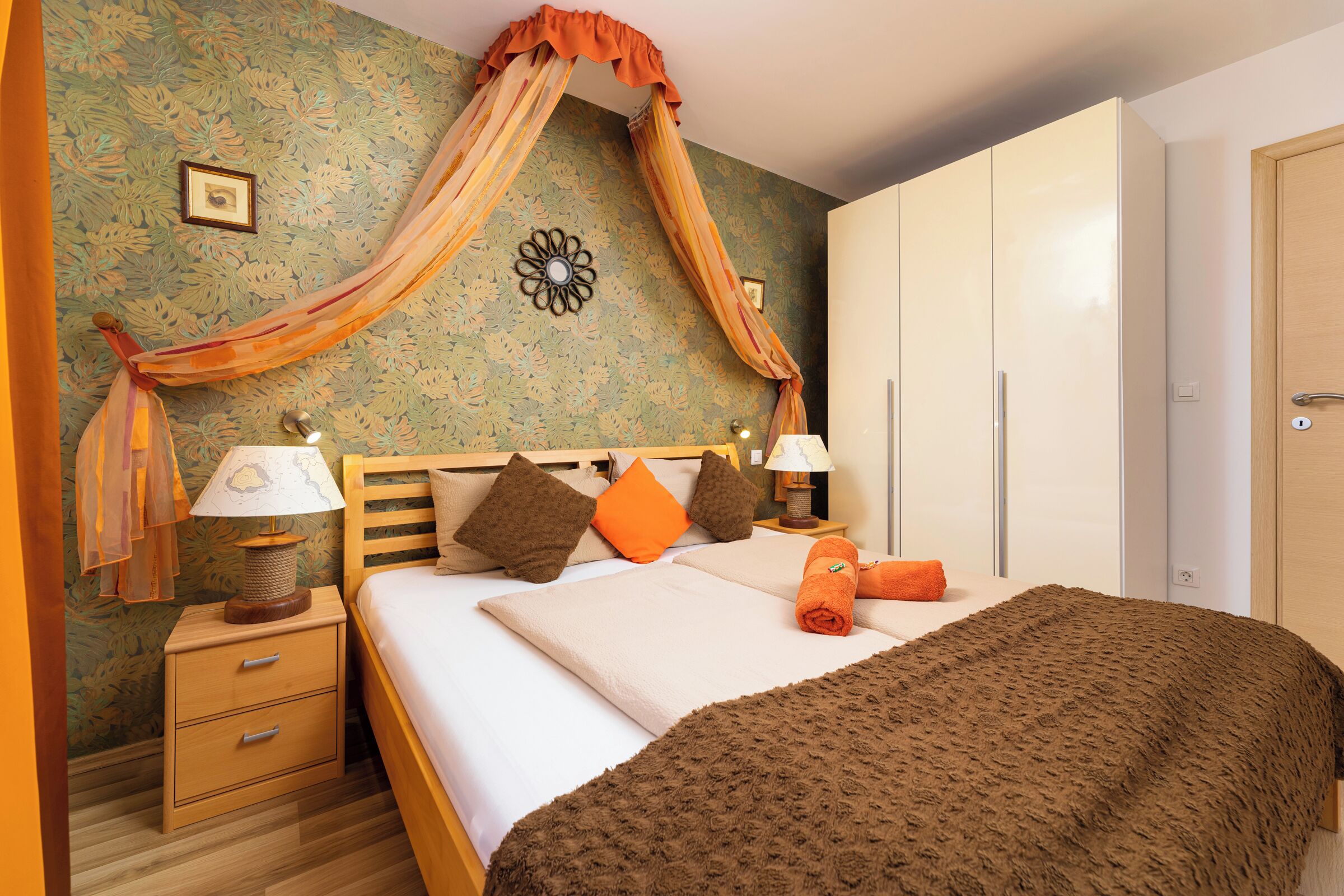 A bedroom with a bed, nightstands, a wardrobe, and a decorative wall.