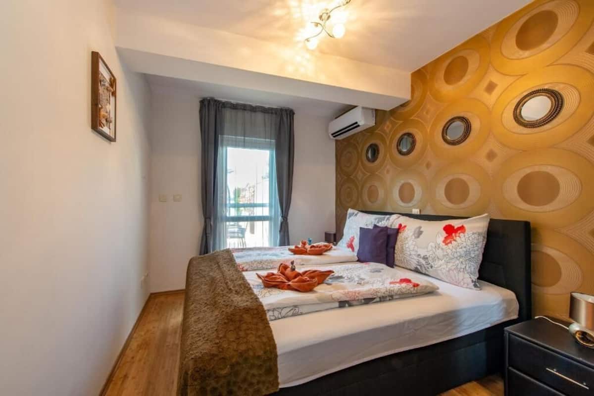 A hotel room with a bed, a bedside table, a window with curtains, and a patterned wall.
