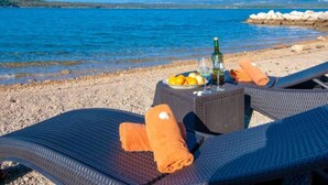 A beachside lounge with wicker chairs, a table with a bottle, glasses, and fruit. - Soline Bay Seashore Residence (Dobrinj)