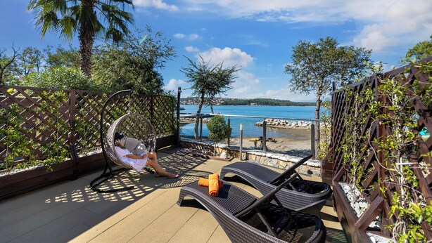 A balcony with wicker chairs, a hanging chair, and a view of the beach and sea. - Soline Bay Seashore Residence (Dobrinj)