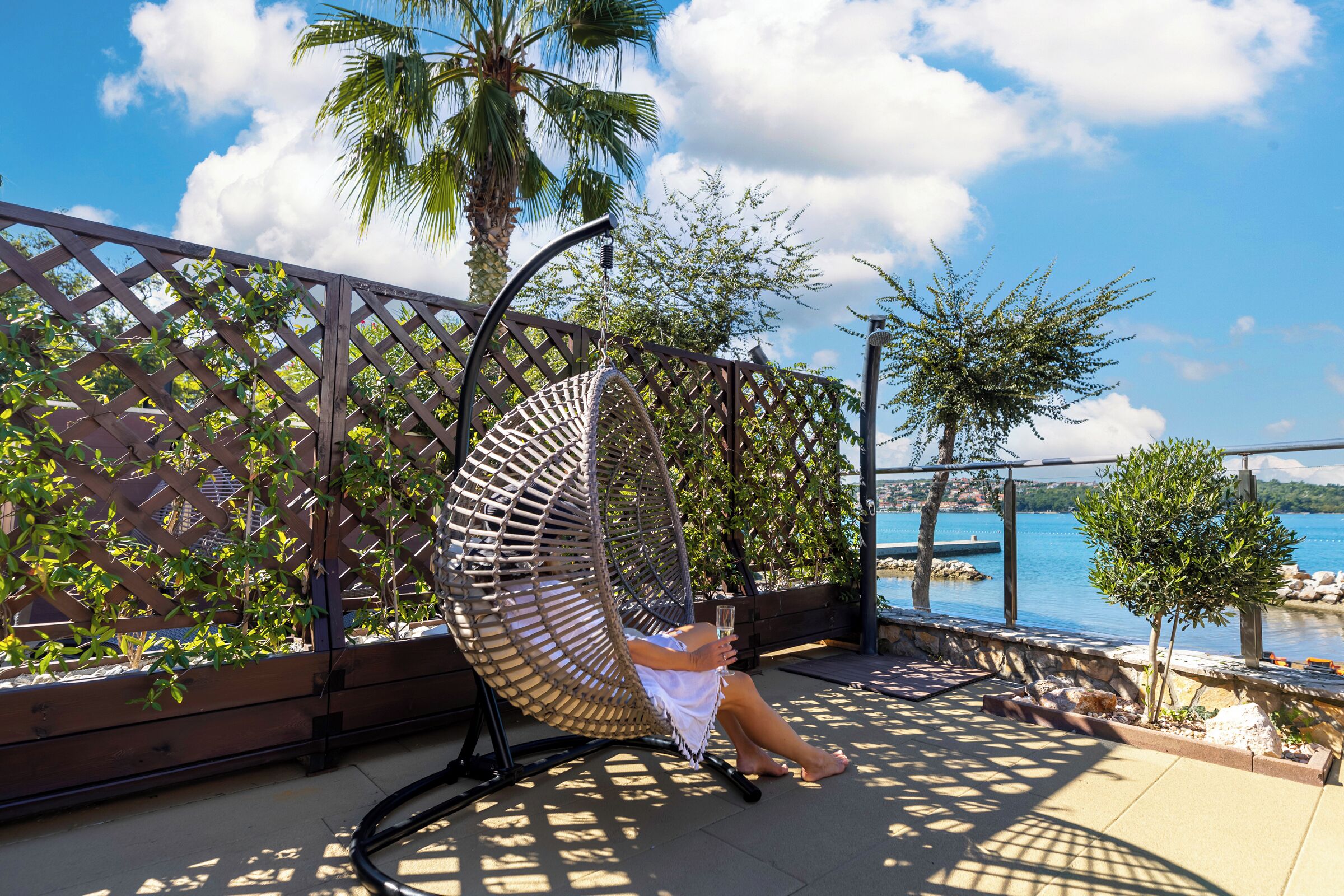 Una persona relajándose en una silla de mimbre en un balcón con vistas al mar.