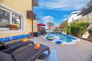 Uma área com espreguiçadeiras, guarda-sóis e piscina.