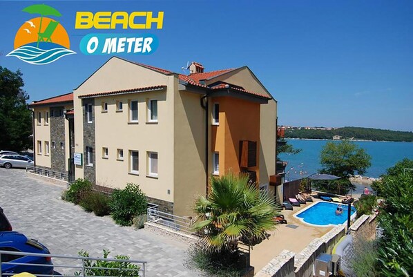 Um edifício de dois andares com piscina, vista para a praia e céu claro.