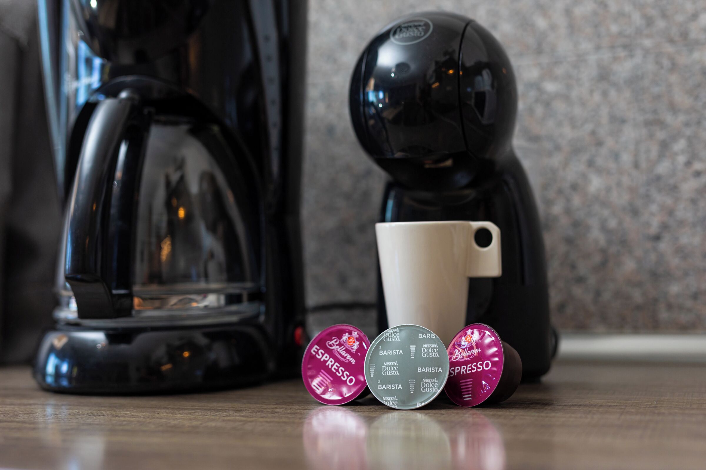 A coffee maker, a cup, and three capsules labeled with different coffee types.