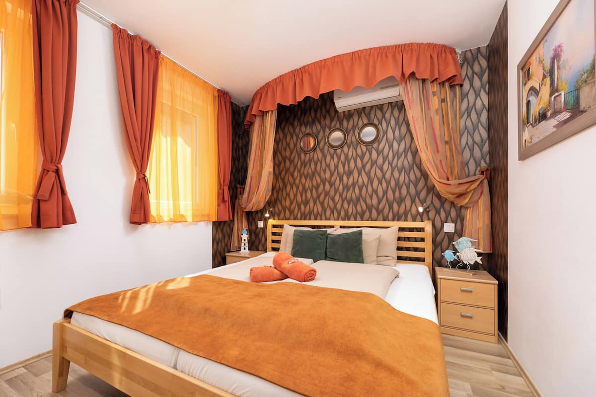 A neatly made bed with a brown blanket, a wooden headboard, and a nightstand with a lamp.