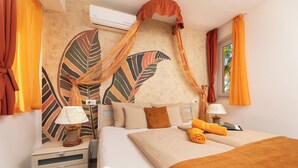 A neatly made bed with a brown blanket, a wooden nightstand with a lamp, and a wall with a large leaf pattern. - Soline Bay Seashore Residence (Dobrinj)