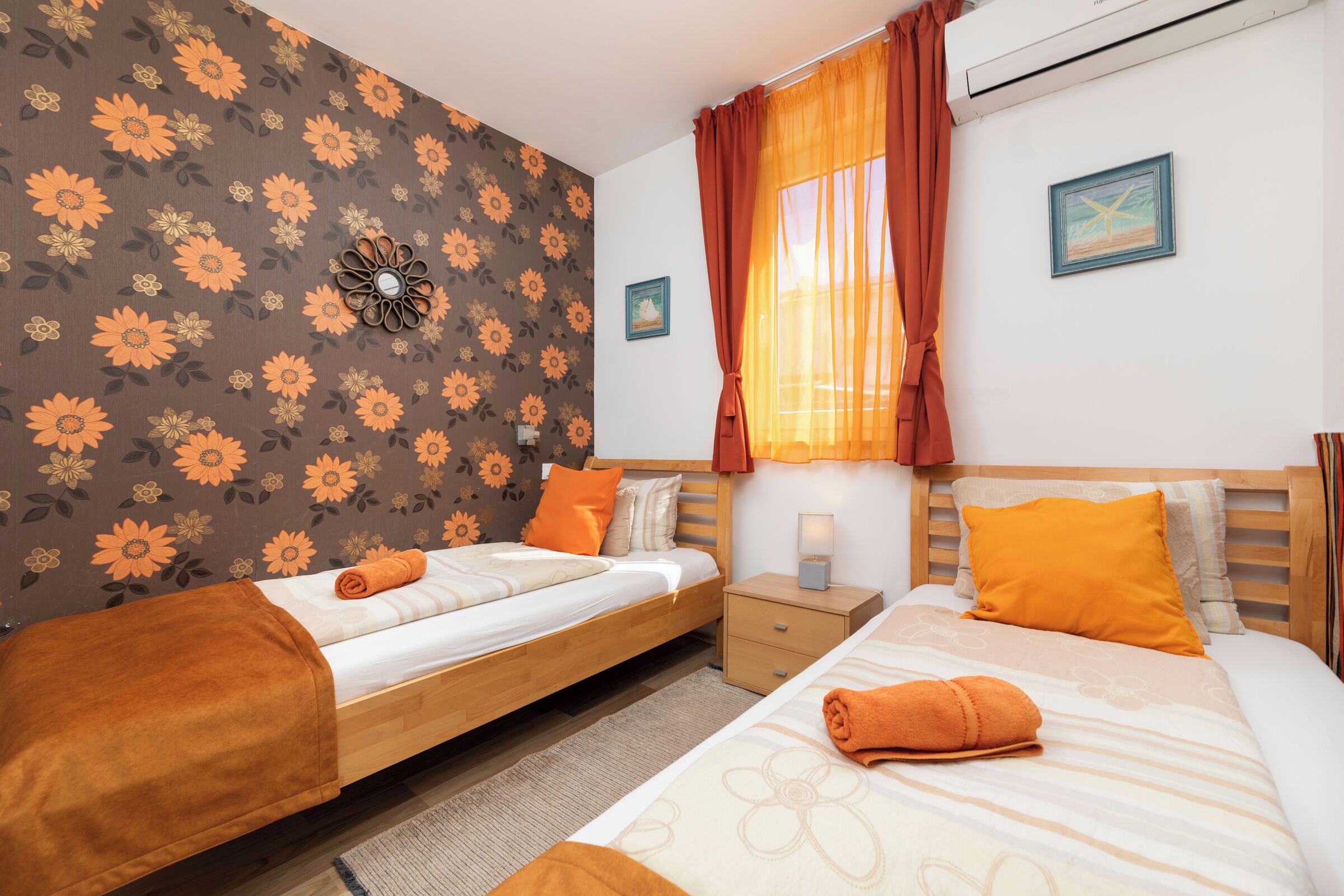A hotel room with two beds, a nightstand, a wall clock, and a window with curtains.